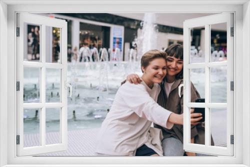 Two girls take a selfie in the mall, a fountain in the background