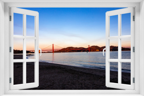 Fototapeta Naklejka Na Ścianę Okno 3D - Sunset over San Francisco Bay, California with the red Golden Gate Bridge and mountains in the background and wave and light reflecting in the water in the foreground, horizontal image