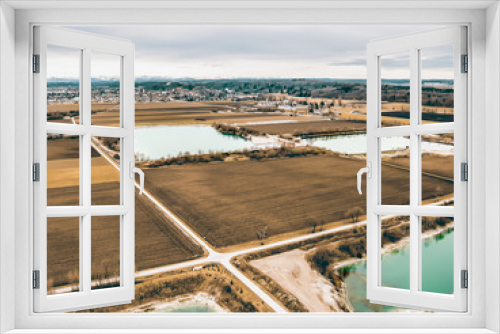 Fototapeta Naklejka Na Ścianę Okno 3D - Drohnenbild, Luftaufnahme Felder und Seen vor einer Ortschaft mit Alpenblick und bewölktem Himmel
