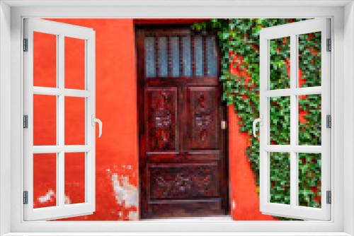 Fototapeta Naklejka Na Ścianę Okno 3D - A red varnished door with an orange wall and a green ivy on the one side