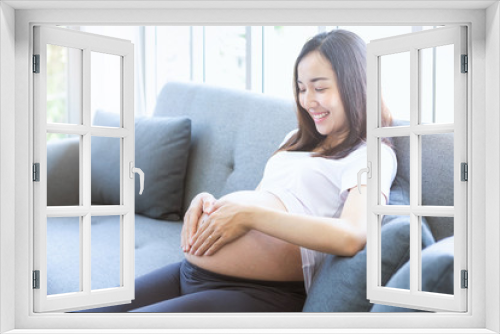 Mothers wearing wedding rings are making heart-shaped hands on their pregnant belly.