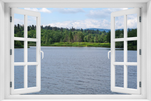 Fototapeta Naklejka Na Ścianę Okno 3D - Mountain lake with cold dark water surrounded by green forest under a blue sky on a sunny day