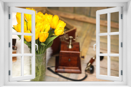 Fototapeta Naklejka Na Ścianę Okno 3D - A bouquet of yellow tulips in a vase in the interior of a retro room. Retro interior with bouquet of tulips old phone and suitcase.