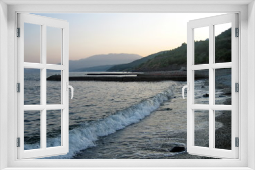 Fototapeta Naklejka Na Ścianę Okno 3D - Breakwater on the shore of a calm sea against the background of coastal mountains in the haze of the sky in the distance in the evening.