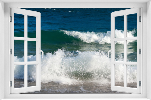 Fototapeta Naklejka Na Ścianę Okno 3D - During windy days, the water of Lake Garda reaches the shore forming frothy and shiny waves that break and stretch on the pebble beach. In autumn the water has a very dark blue color. Italy.