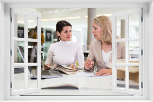 Friendly female tutor helping to diligent positive girl preparing for exam in library