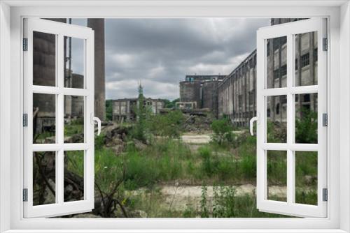 Fototapeta Naklejka Na Ścianę Okno 3D - An abandoned, overgrown industrial estate, with tall pipes, ruined buildings, weeds and piles of rubbish