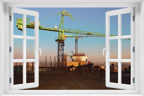 Fototapeta Naklejka Na Ścianę Okno 3D - The construction of a rooftop high rise building, workers are tied with steel bars for concrete pouring, surveying the site and cranes are lifting or moving metal at the construction site. Sunset
