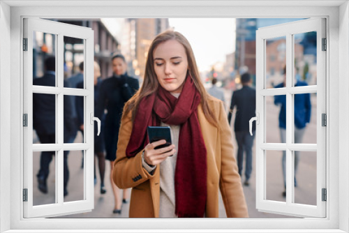 Young Smart Casually Dressed Female is Using a Smartphone on a Street. Business People and Office Managers Walk Pass on Their Way to Work. She Looks Confident while Checking Her Cell and Walking.