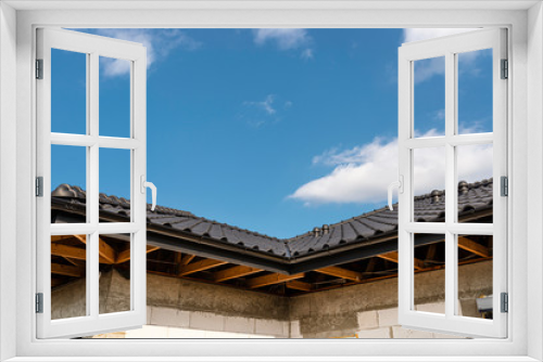 Fototapeta Naklejka Na Ścianę Okno 3D - The roof of a single-family house covered with a new ceramic tile in anthracite against the blue sky, visible trusses.
