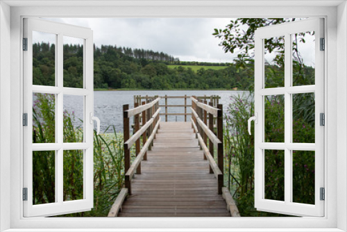 Fototapeta Naklejka Na Ścianę Okno 3D - Wooden bridge facing the lake in a green scenery