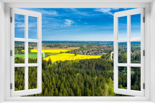 Fototapeta Naklejka Na Ścianę Okno 3D - Birds eye view over a green forest to a big rapeseed field in front of a village at the horizon. Beautiful day in spring in southern germany,