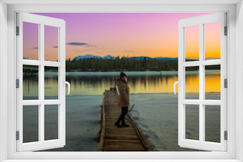 Fototapeta Naklejka Na Ścianę Okno 3D - Woman standing on a pier, boat launch with snow & purple, orange and pink stunning sunset with mountains and river, lake reflection. 