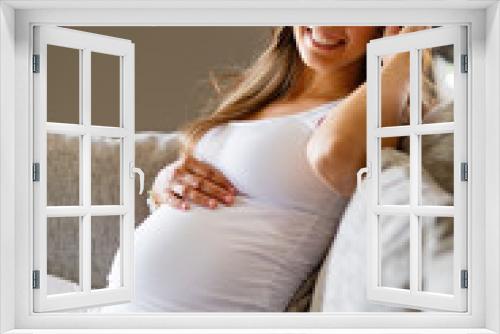 Happy beautiful pregnant woman sitting in sofa touching her belly