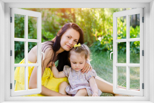 Mom and daughter in the summer park. Mom in a yellow dress and daughter with a bow on her head toy hug and laugh in the sun