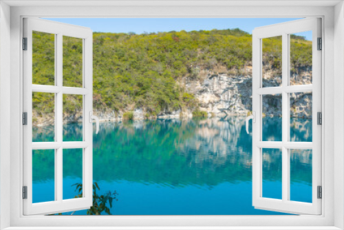 Fototapeta Naklejka Na Ścianę Okno 3D - View of the Cenote of Candelaria in Huehuetenango, Guatemala, on a sunny day where you can see the turquoise color of the water and the reflection of the trees in the water.