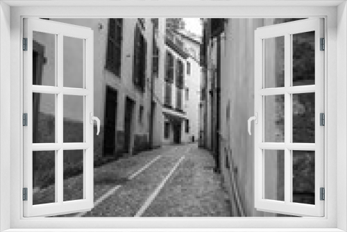 Fototapeta Naklejka Na Ścianę Okno 3D - A narrow European street isolated in the period of pandemic covid-19. Black and white photo of deserted narrow street with old architecture in the period of self-isolation. Paving stones. Stay home