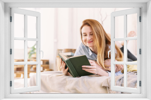 Lovely woman reading a book, lying in bed. A young adult girl is studying at home alone