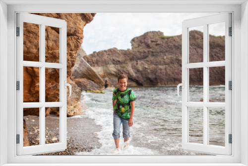 Fototapeta Naklejka Na Ścianę Okno 3D - Happy hamdsome teen walks along the sea coast against the background of the sea, from behind a beautiful landscape