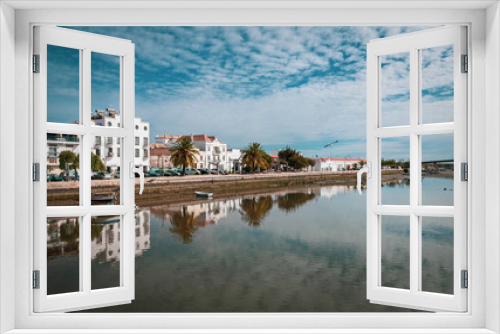 Fototapeta Naklejka Na Ścianę Okno 3D - Reflection of cloudy sky and Tavira embankment in the water of the Gilao River, Algarve, Portugal