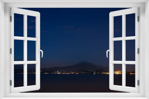 Fototapeta Naklejka Na Ścianę Okno 3D - Night shot from a coast of Peschiera del Garda to the Garda lake and mountains with lights all over the other coast. Lights of Garda town in the night from other coast.