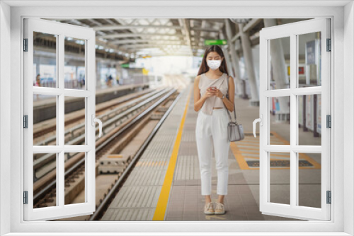 Young Asian woman passenger wearing surgical mask and using social network via smart mobile phone in subway train when traveling in big city