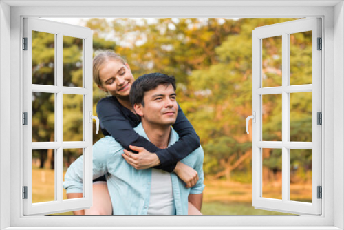 Pretty girl is riding on back of handsome guy in park.