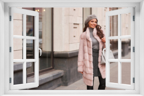 Beautiful caucasian woman with long brunette hair in pink fur coat and gray beret walking in city. Outdoor portrait. Fashionable luxury rich girl