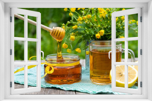 Fototapeta Naklejka Na Ścianę Okno 3D - Dripping honey from a wooden spoon with a Cup of tea and lemon on a background of greenery and a bouquet of field yellow flowers.