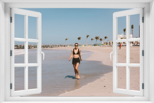 Fototapeta Naklejka Na Ścianę Okno 3D - Happy slim girl goes in the bikini, glasses and shorts on the beach
