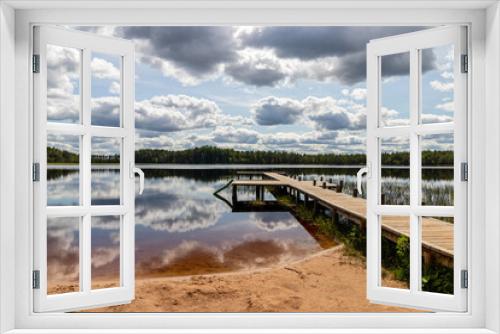 Fototapeta Naklejka Na Ścianę Okno 3D - Landscape with a swamp lake and with a wooden footbridge. Beautiful clouds and the surrounding forest were reflected in dark water. Latvia. Lake Ratnieku