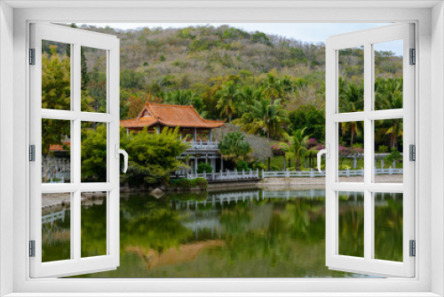 Fototapeta Naklejka Na Ścianę Okno 3D - Green lake surrounded by gazebos, temples, mountains, flowers, palm grove and stone fence on the territory of Buddhist center Nanshan.