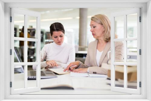 Female teacher working with girl student in university library