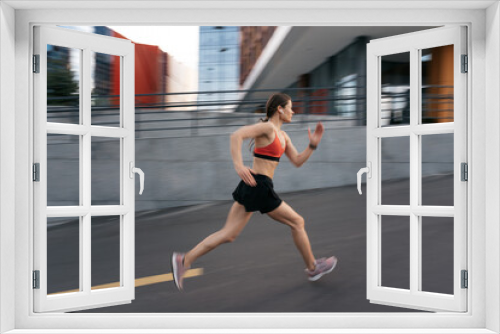 Young woman sprinting in the morning outdoors. Side view of female runner in motion working out in the city.