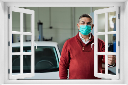 Mid adult man wearing protective face mask while holding car key in auto repair shop.