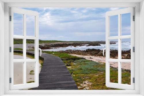 Fototapeta Naklejka Na Ścianę Okno 3D - Wooden boardwalk near the rocky coast and blue ocean with waves on the windy day at Cape Agulhas, the most southern point of Africa, where the Indian and Atlantic oceans meet, South Africa
