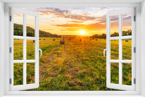 Fototapeta Naklejka Na Ścianę Okno 3D - Scenic view at beautiful sunset in a green shiny field with hay stacks, bright cloudy sky , trees and golden sun rays with glow, summer valley landscape