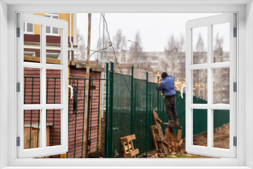 Fototapeta Naklejka Na Ścianę Okno 3D - A man cuts a metal fence with a saw. A worker installs a new fence.