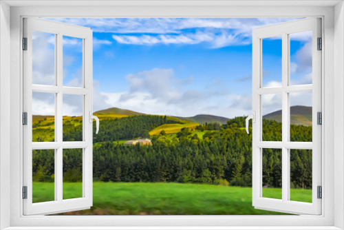 Fototapeta Naklejka Na Ścianę Okno 3D - View of the pastoral rural landscape with mountains, forest and blue sky from the window of a traveling car.