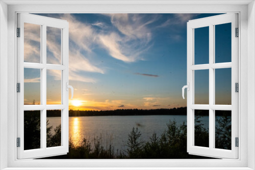 Fototapeta Naklejka Na Ścianę Okno 3D - Panorama of a gorgeous sunset at a forest lake, with gold and blue color in the sky and trees reflected in the water. High quality photo