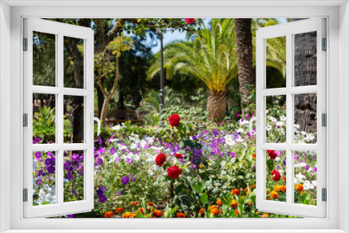 Fototapeta Naklejka Na Ścianę Okno 3D - Flowery garden with petunias, roses, palm trees and other trees. Multicolor, beautiful landscape in Spanish garden