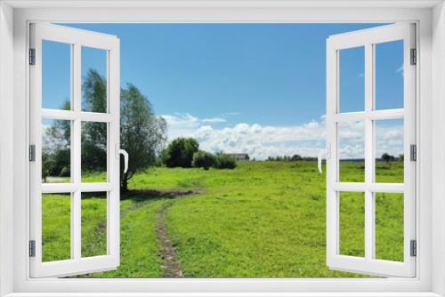 Fototapeta Naklejka Na Ścianę Okno 3D - country road to the village through a green field on a sunny day against a blue sky