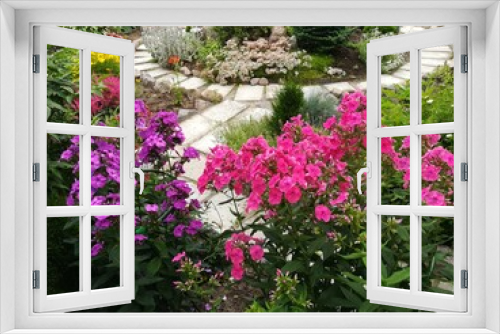Fototapeta Naklejka Na Ścianę Okno 3D - beautiful blooming pink and purple Phlox on a flower bed on the background of a round hill with coniferous plants and a paved path. Summer day in the village. Flower Wallpaper