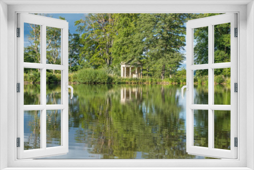 Fototapeta Naklejka Na Ścianę Okno 3D - A view across a beautiful lake with reflections of trees towards an old abandoned structure in the middle of a rural countryside scene