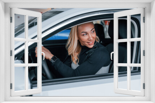 Side view of beautiful blonde in elegant clothes that sitting inside of modern car