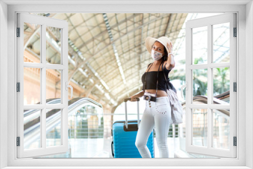 Tourist woman with luggage and travel accessories on the escalator of a transport station. She wears a face mask as a preventive measure. Space for text. Safe travel concept.