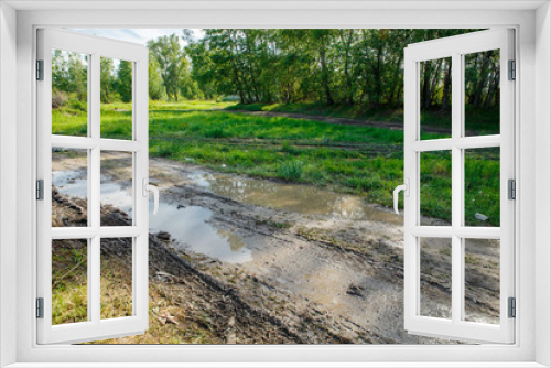 Fototapeta Naklejka Na Ścianę Okno 3D - The harsh landscape nature and road through the fields for the off-road SUV with puddles and mud. Autumn or spring background. Forest in the background. Rain-washed road, is impassable, slush, mud