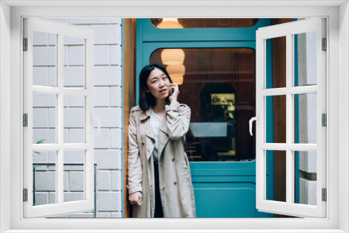 Positive modern Asian woman speaking on smartphone on street