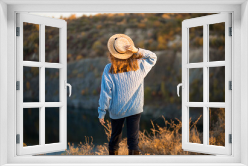 Fototapeta Naklejka Na Ścianę Okno 3D - Autumn girl in blue sweater and hat standing backwards and admire nature lake view. Autumn forest colors with girl back view.