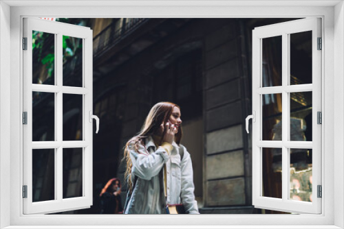 Joyful modern female student talking on smartphone while walking along street